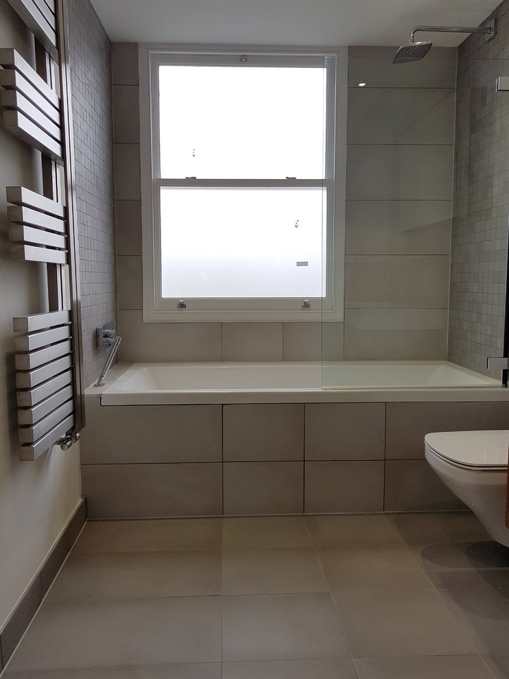 Medium sized contemporary family bathroom in London with medium wood cabinets, a built-in bath, a shower/bath combination, a wall mounted toilet, grey tiles, porcelain tiles, grey walls, porcelain flooring, a wall-mounted sink and tiled worktops.