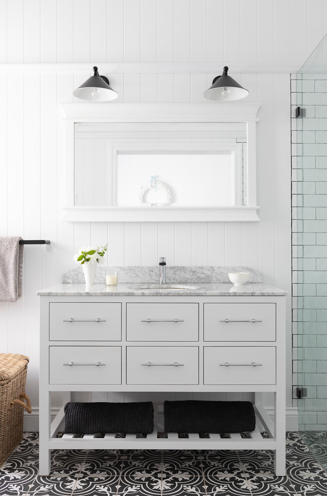 Foto på ett lantligt vit badrum, med vita skåp, en kantlös dusch, vit kakel, tunnelbanekakel, vita väggar, ett undermonterad handfat, flerfärgat golv och släta luckor