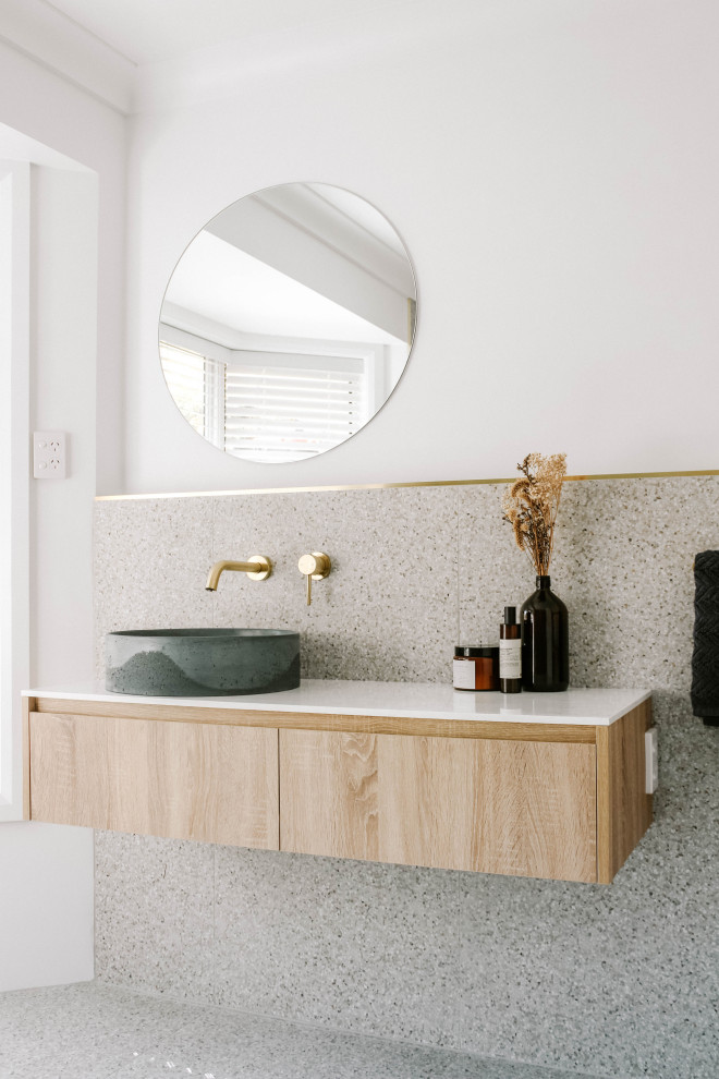 Idéer för industriella vitt en-suite badrum, med vita väggar, ett fristående handfat, granitbänkskiva, keramikplattor, terrazzogolv, släta luckor, skåp i ljust trä, grå kakel och grått golv