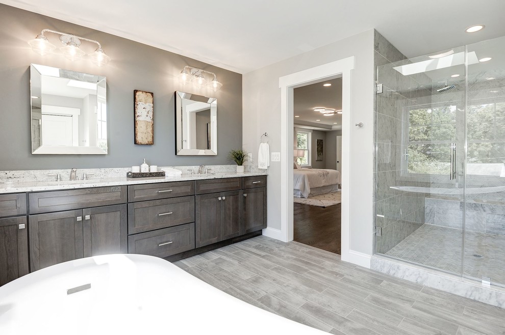 Exemple d'une salle de bain principale craftsman de taille moyenne avec un placard à porte shaker, des portes de placard grises, une baignoire indépendante, un mur gris, un sol en carrelage de porcelaine, un lavabo encastré, un plan de toilette en quartz modifié et un sol gris.