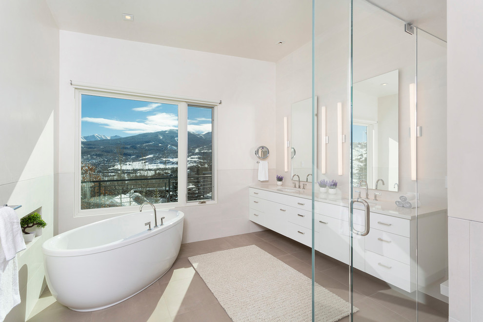 На фото: большая главная ванная комната в современном стиле с плоскими фасадами, белыми фасадами, отдельно стоящей ванной, белой плиткой, белыми стенами, полом из керамической плитки и серым полом