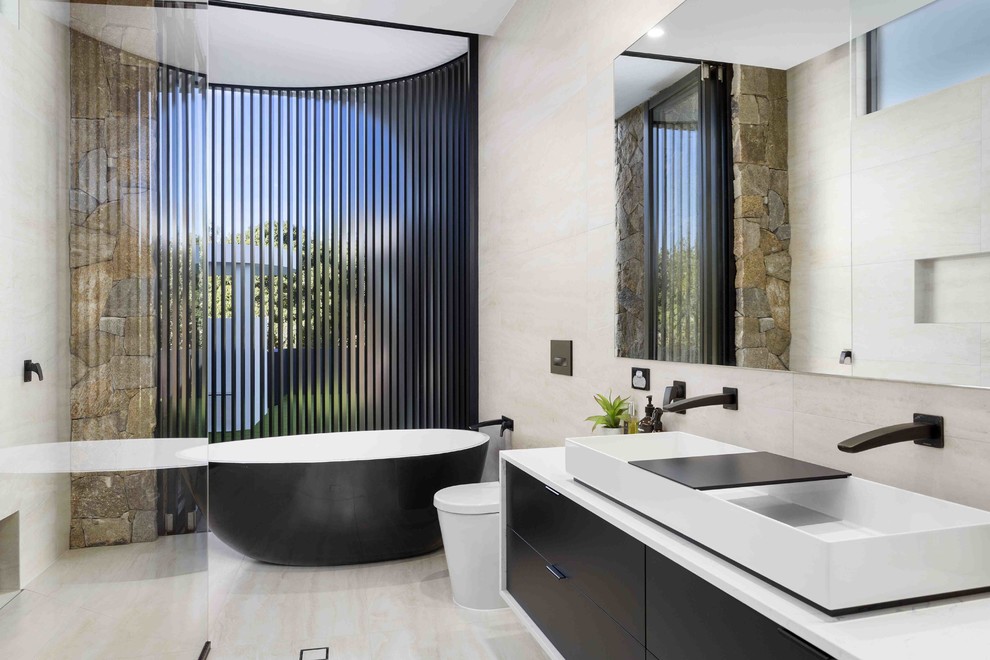 Inspiration for a contemporary ensuite bathroom in Gold Coast - Tweed with flat-panel cabinets, black cabinets, a freestanding bath, a walk-in shower, a one-piece toilet, beige tiles, beige walls, a trough sink, concrete worktops, beige floors, an open shower and grey worktops.
