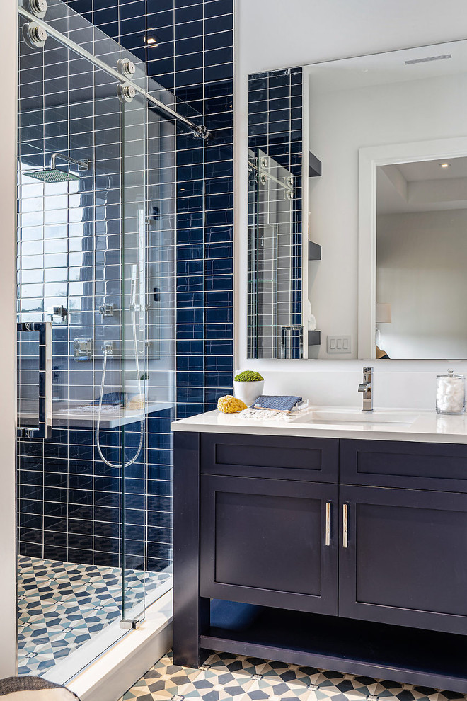 Cette image montre une salle de bain marine avec des portes de placard bleues, un carrelage bleu, un mur blanc, un lavabo encastré, un sol multicolore, une cabine de douche à porte coulissante, un plan de toilette blanc, carreaux de ciment au sol et un placard à porte shaker.