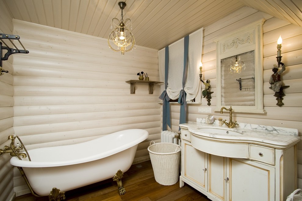 На фото: главная ванная комната в деревянном доме в стиле кантри с искусственно-состаренными фасадами, ванной на ножках, белыми стенами, врезной раковиной и мраморной столешницей