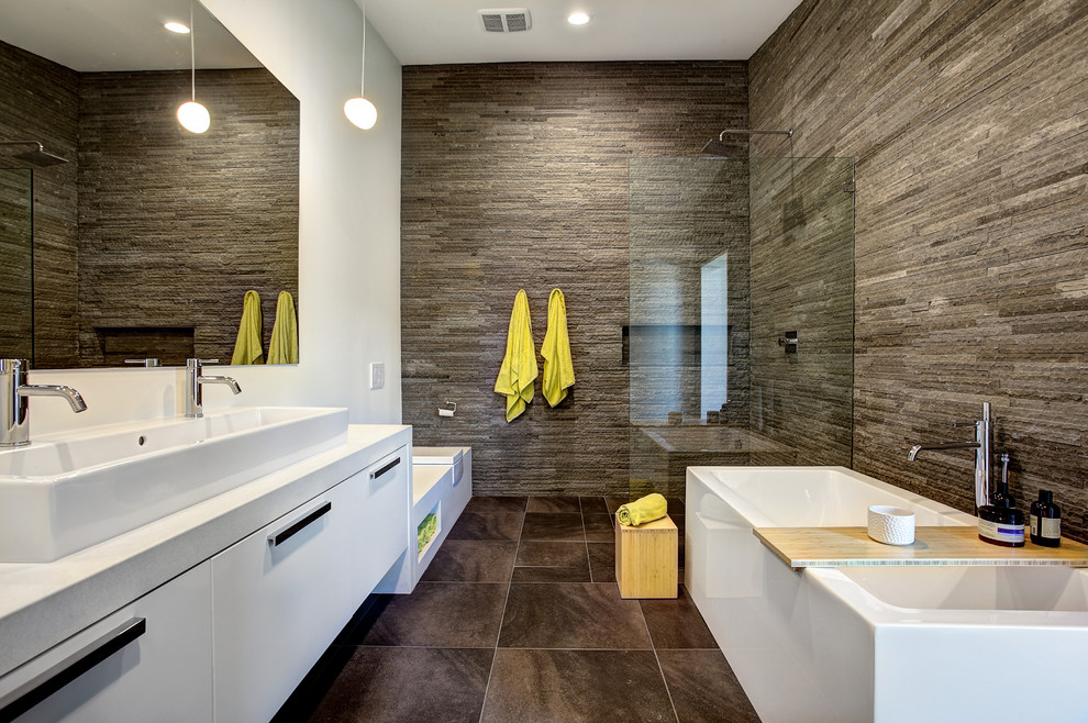 Bild på ett stort funkis en-suite badrum, med ett avlångt handfat, släta luckor, vita skåp, ett fristående badkar, stenkakel, vita väggar, en kantlös dusch, en vägghängd toalettstol och grå kakel