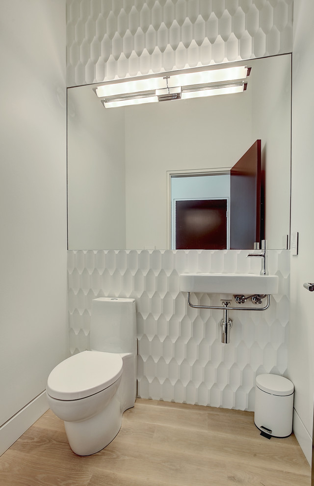 This is an example of a small contemporary cloakroom in Grand Rapids with a wall-mounted sink, white walls, light hardwood flooring and a one-piece toilet.