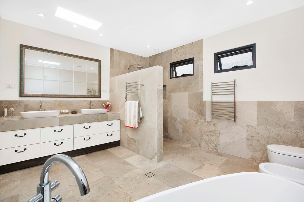 シドニーにある広いコンテンポラリースタイルのおしゃれなマスターバスルーム (ベッセル式洗面器、フラットパネル扉のキャビネット、白いキャビネット、置き型浴槽、アルコーブ型シャワー、ベージュのタイル、セラミックタイル、白い壁、セラミックタイルの床) の写真