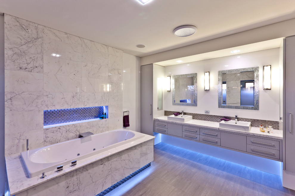 Example of a large minimalist master white tile and porcelain tile limestone floor drop-in bathtub design in Perth with flat-panel cabinets, white cabinets, quartz countertops and white walls