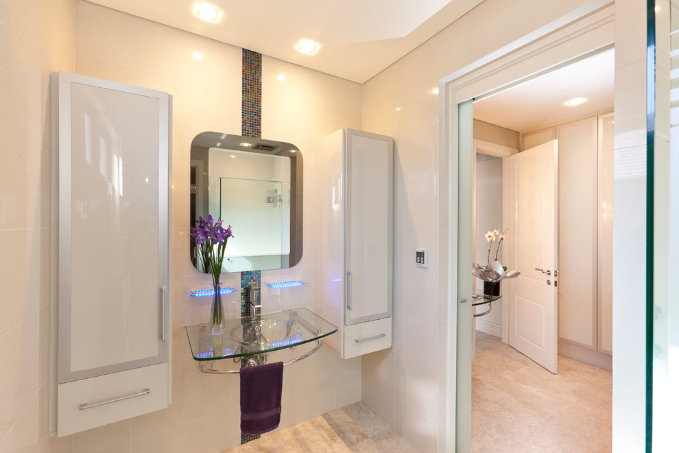 Inspiration pour une salle de bain minimaliste de taille moyenne pour enfant avec un lavabo suspendu, un placard à porte vitrée, un plan de toilette en verre, un carrelage beige, un mur beige et un sol en calcaire.