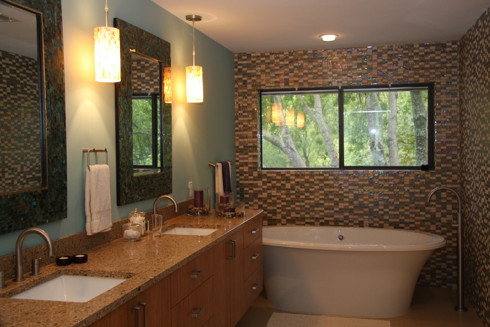 На фото: ванная комната в современном стиле с врезной раковиной, плоскими фасадами, светлыми деревянными фасадами, столешницей из искусственного кварца, отдельно стоящей ванной, разноцветной плиткой и стеклянной плиткой с