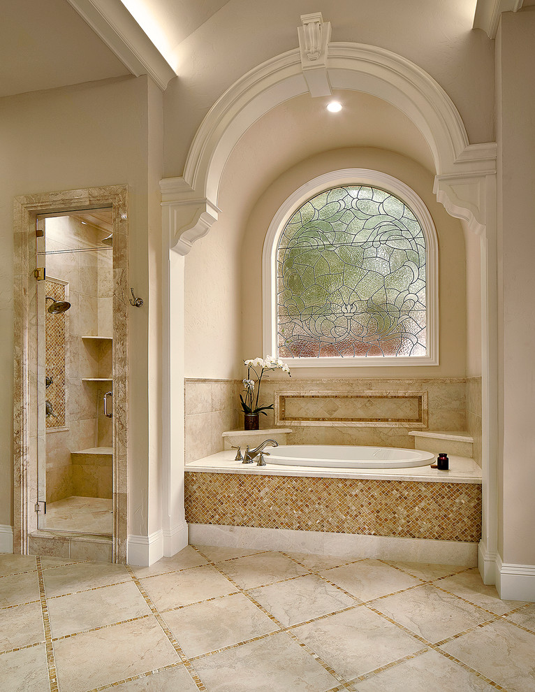Cette image montre une très grande salle de bain principale traditionnelle avec des portes de placard beiges, une baignoire posée, une douche d'angle, un carrelage beige, des carreaux de porcelaine, un mur beige, un sol en carrelage de céramique, un lavabo encastré et un plan de toilette en marbre.