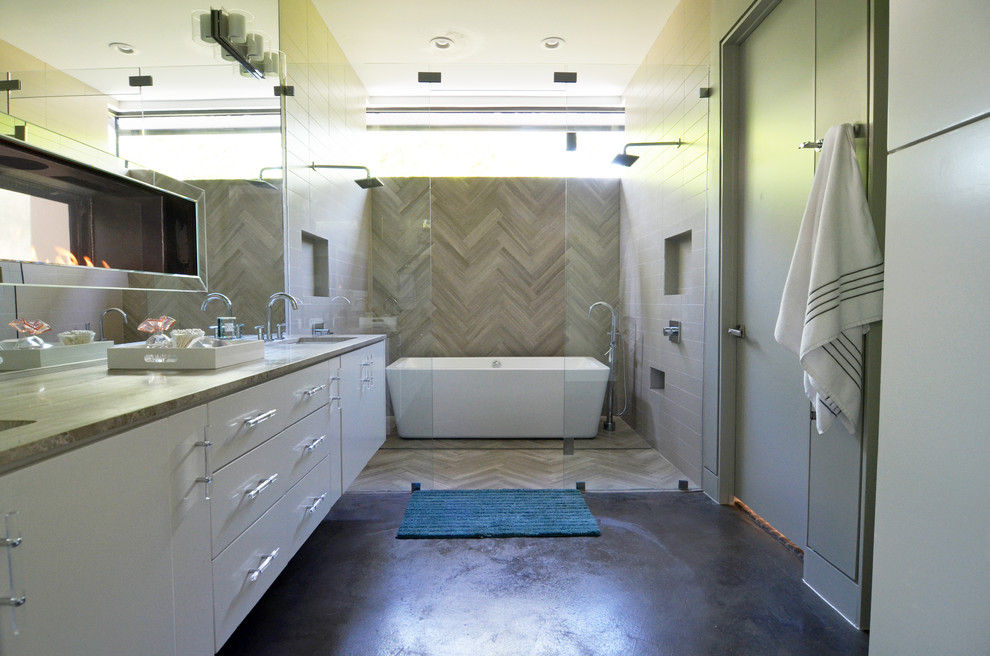 На фото: главная ванная комната в современном стиле с врезной раковиной, плоскими фасадами, белыми фасадами, отдельно стоящей ванной, двойным душем, серой плиткой, бетонным полом и бежевыми стенами с