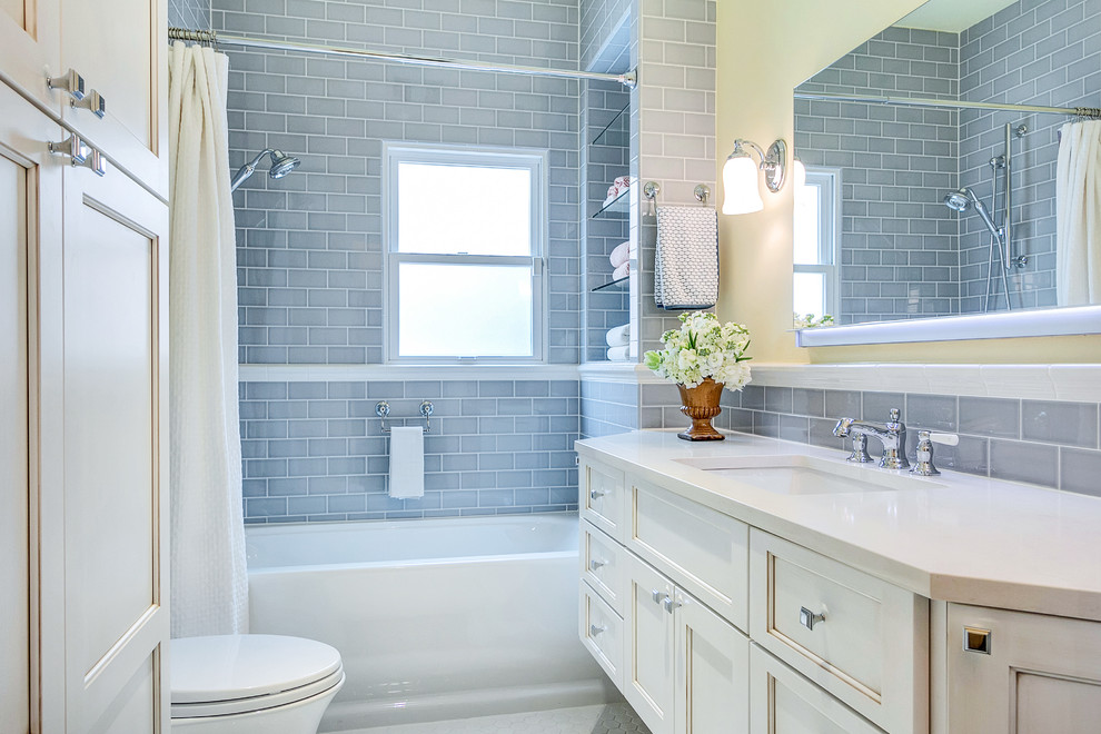 Klassisk inredning av ett litet badrum, med ett undermonterad handfat, luckor med infälld panel, vita skåp, bänkskiva i kvarts, ett badkar i en alkov, en dusch/badkar-kombination, en vägghängd toalettstol, grå kakel, keramikplattor, vita väggar och klinkergolv i keramik