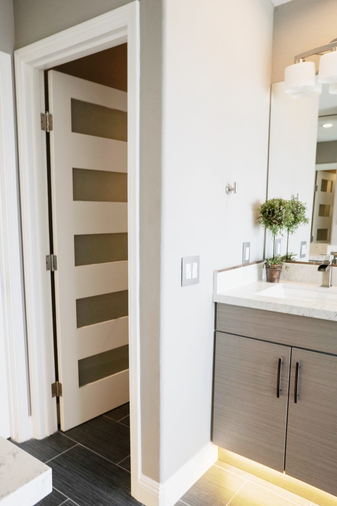 This is an example of a medium sized modern ensuite bathroom in Orange County with flat-panel cabinets, beige cabinets, a freestanding bath, a shower/bath combination, a one-piece toilet, porcelain tiles, porcelain flooring, a built-in sink, engineered stone worktops, black floors and a hinged door.