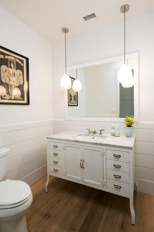 White bathroom vanity cabinet with marble countertop, under-mount sink, chrome faucet, and multiple drawers, paired with a large wall mirror and pendant lights in a modern bathroom.
