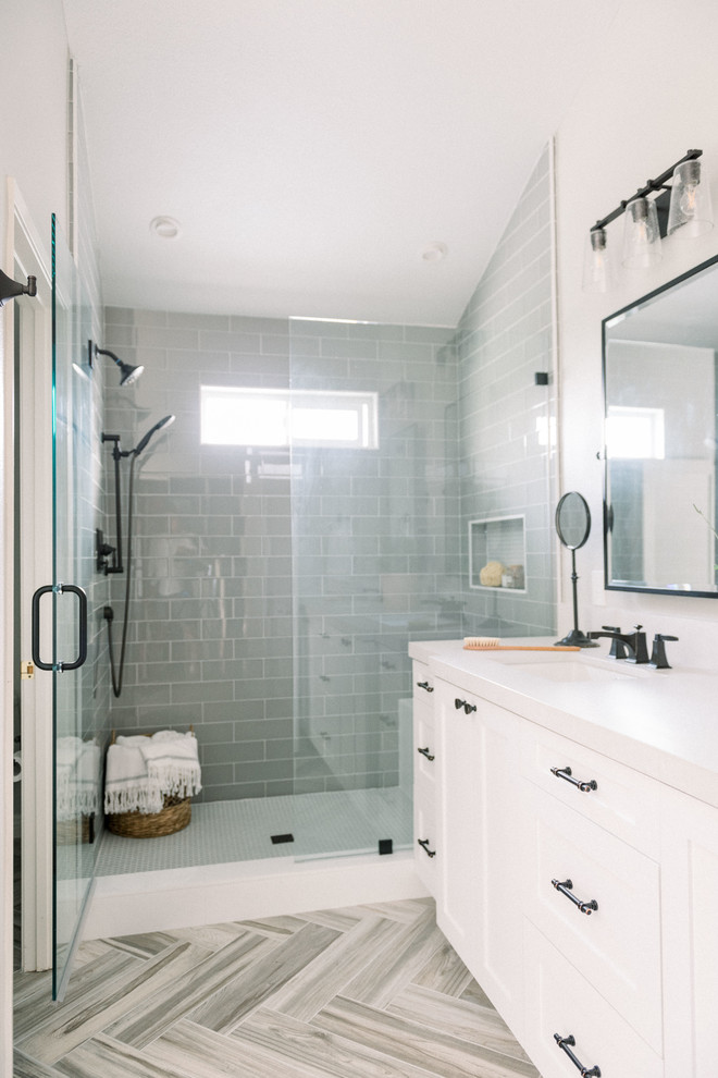 Foto de cuarto de baño principal campestre de tamaño medio con armarios estilo shaker, puertas de armario blancas, ducha empotrada, sanitario de una pieza, baldosas y/o azulejos grises, baldosas y/o azulejos de vidrio, paredes grises, suelo de baldosas de porcelana, lavabo bajoencimera, encimera de cuarzo compacto, suelo beige, ducha con puerta con bisagras y encimeras blancas