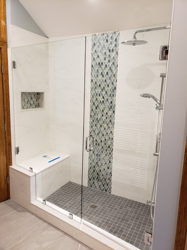 This is an example of a medium sized contemporary ensuite bathroom in Boston with raised-panel cabinets, medium wood cabinets, an alcove shower, a bidet, white tiles, marble tiles, blue walls, ceramic flooring, a submerged sink, engineered stone worktops, grey floors, a hinged door, white worktops, a laundry area, double sinks, a built in vanity unit and a vaulted ceiling.