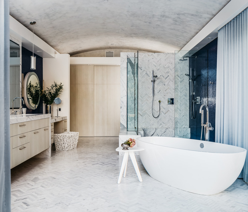 Идея дизайна: большая главная ванная комната в стиле неоклассика (современная классика) с плоскими фасадами, светлыми деревянными фасадами, отдельно стоящей ванной, угловым душем, серой плиткой, мраморной плиткой, белыми стенами, мраморным полом, врезной раковиной, мраморной столешницей, белым полом и душем с распашными дверями