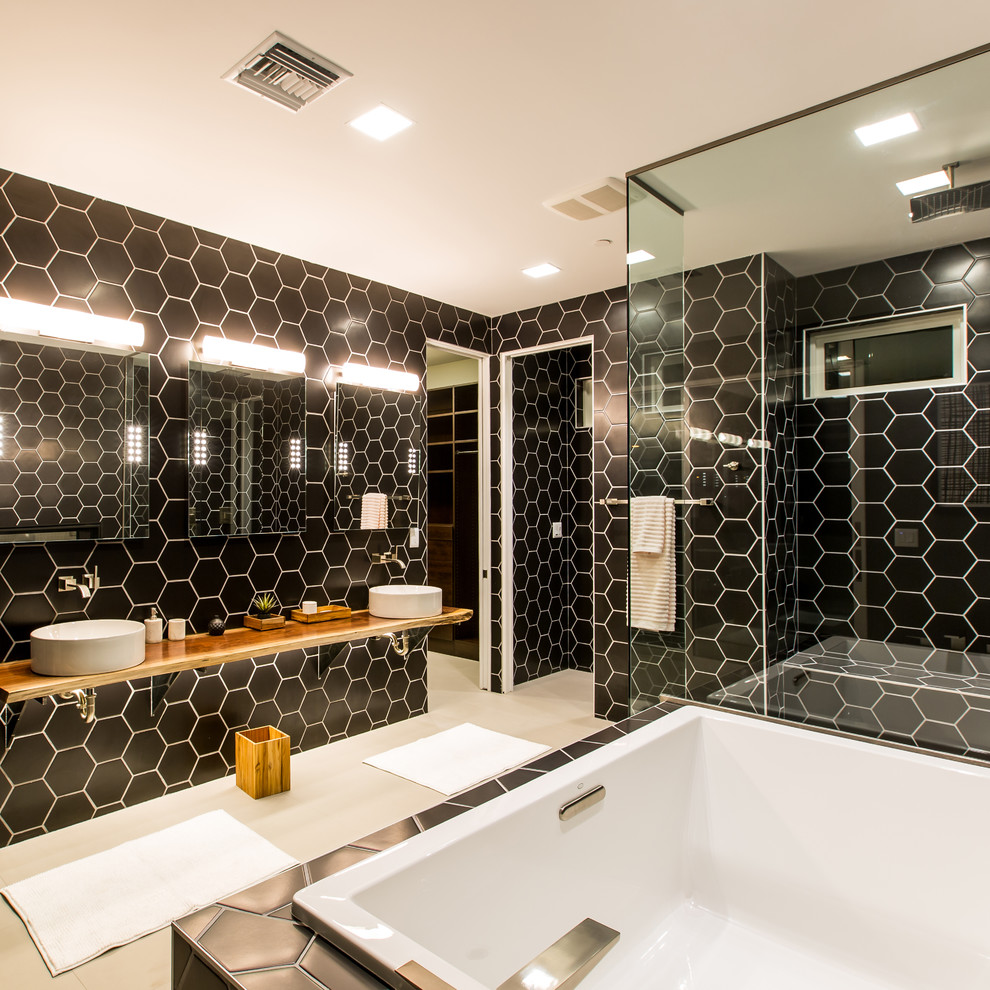 На фото: главная ванная комната в современном стиле с накладной ванной, угловым душем, черной плиткой, черными стенами, настольной раковиной и зеркалом с подсветкой с