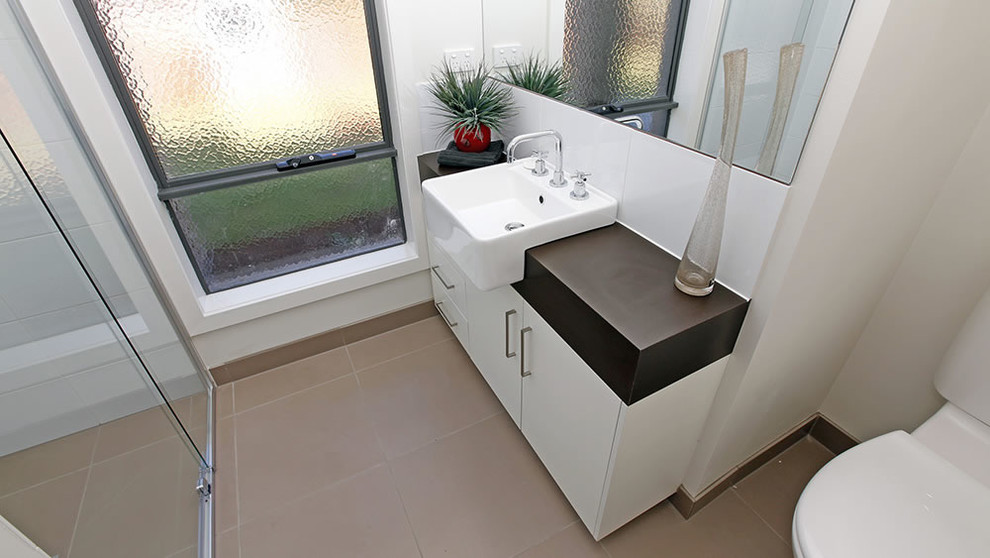 Photo of a small modern family bathroom in Melbourne with beaded cabinets, white cabinets, a corner shower, a one-piece toilet, white tiles, ceramic tiles, white walls, ceramic flooring, a trough sink and solid surface worktops.