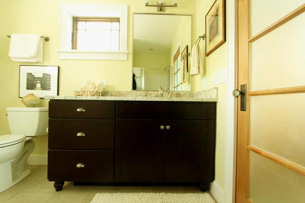 Exemple d'une salle de bain chic en bois foncé de taille moyenne avec WC séparés, un mur jaune, un sol en travertin, un lavabo encastré, un plan de toilette en granite, un placard à porte plane, un carrelage beige et un carrelage de pierre.