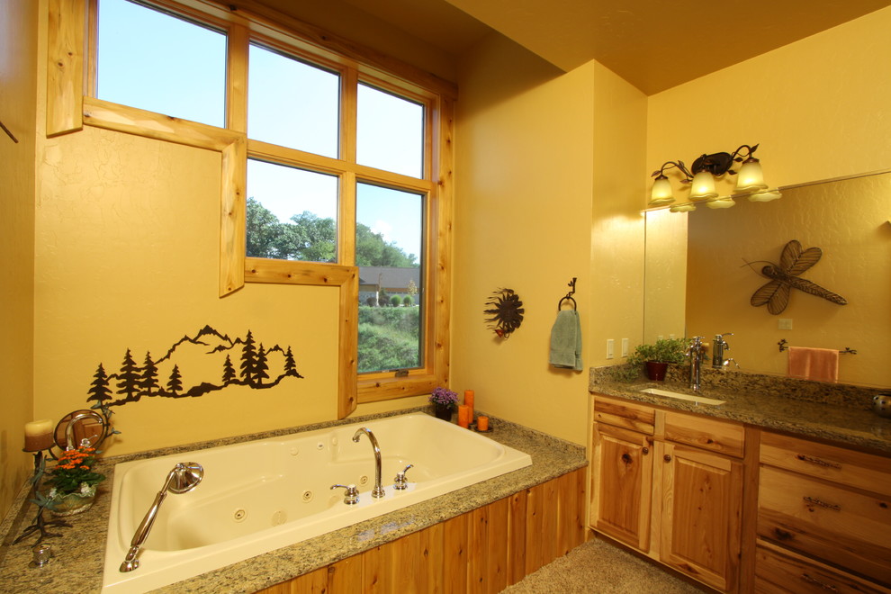 Inspiration pour une salle de bain chalet en bois clair de taille moyenne avec un placard avec porte à panneau surélevé, une baignoire posée, un mur beige, un lavabo encastré et un plan de toilette en granite.