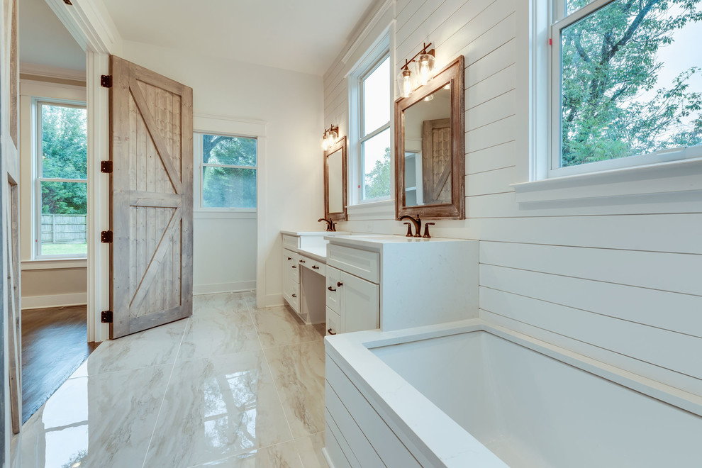Cette image montre une grande salle de bain principale rustique avec un placard à porte shaker, des portes de placard blanches, une baignoire posée, un espace douche bain, WC à poser, un carrelage beige, des carreaux de porcelaine, un mur blanc, un sol en carrelage de porcelaine, un lavabo posé, un plan de toilette en quartz modifié, un sol beige, une cabine de douche à porte battante et un plan de toilette blanc.