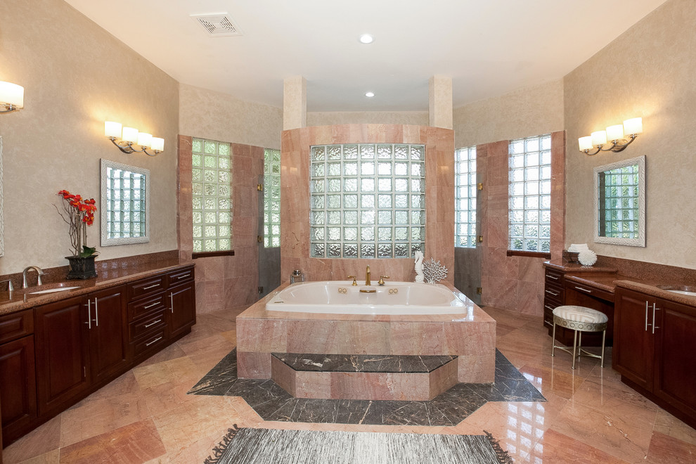 Large traditional ensuite bathroom in Miami with raised-panel cabinets, medium wood cabinets, a built-in bath, beige tiles, pink tiles, travertine tiles, beige walls, travertine flooring, a submerged sink and granite worktops.