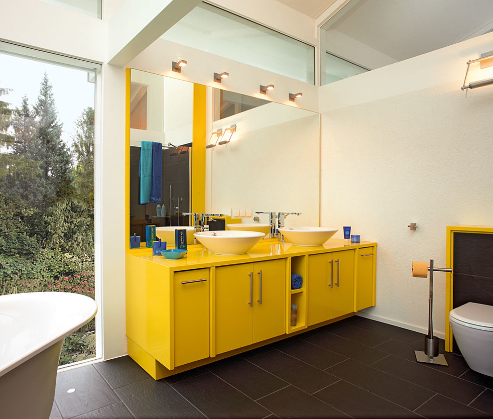 На фото: большая ванная комната в современном стиле с желтыми стенами, желтыми фасадами, отдельно стоящей ванной, черной плиткой и настольной раковиной с