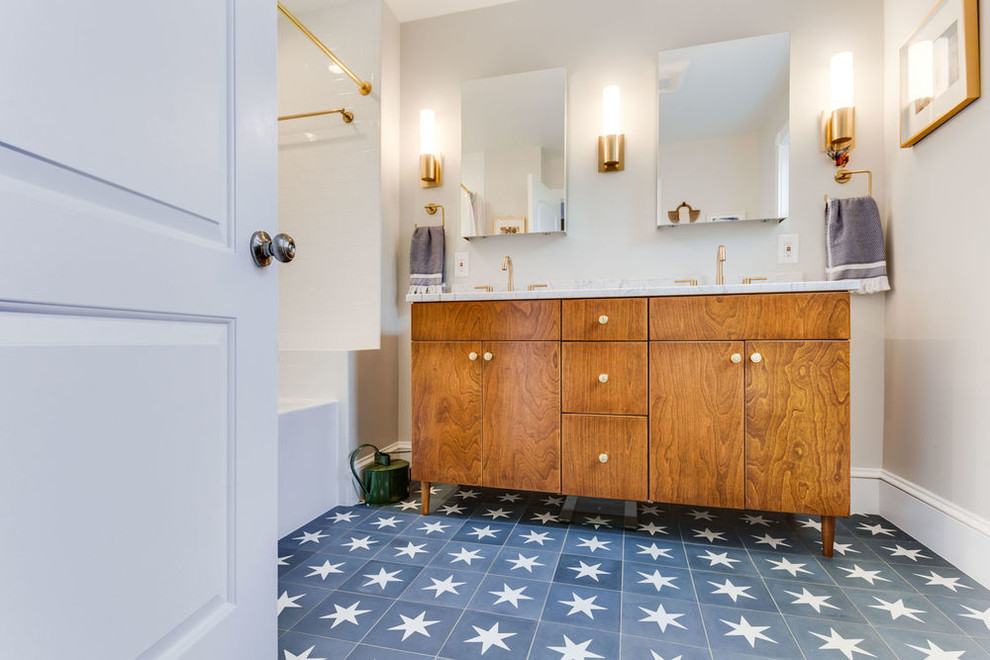 Inredning av ett klassiskt vit vitt badrum, med skåp i mellenmörkt trä, ett badkar i en alkov, vit kakel, cementkakel, cementgolv, ett undermonterad handfat, marmorbänkskiva och blått golv