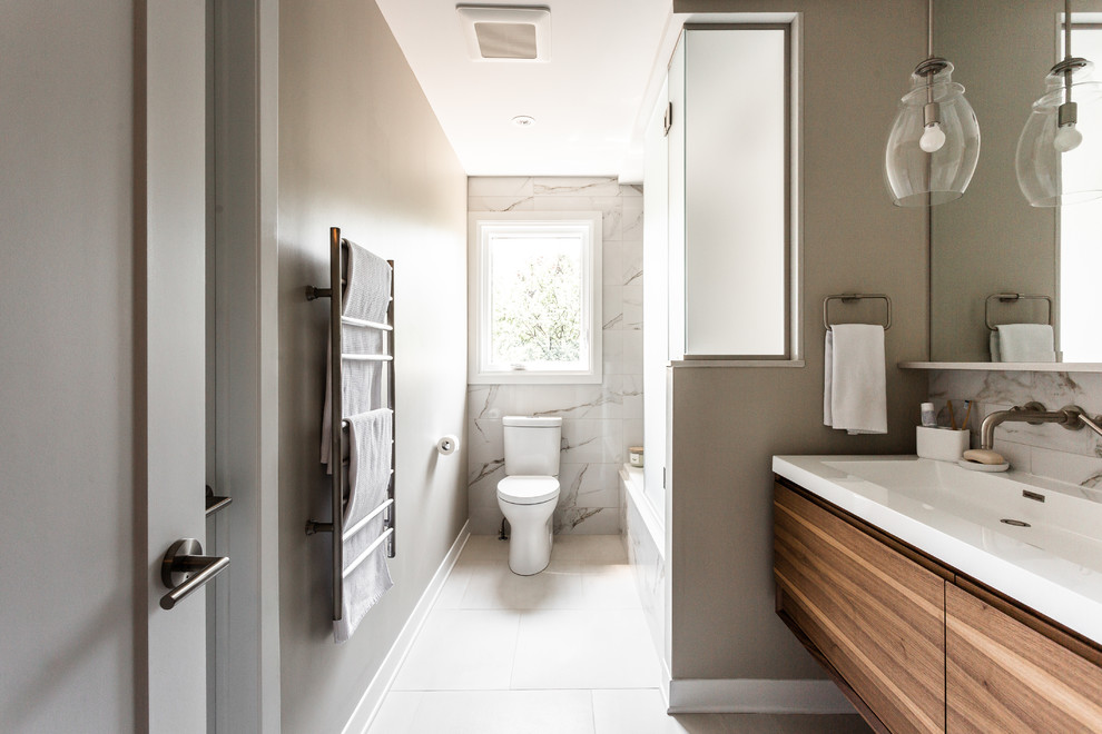 Bild på ett mellanstort funkis vit vitt badrum, med skåp i mellenmörkt trä, ett badkar i en alkov, en dusch/badkar-kombination, en toalettstol med separat cisternkåpa, vit kakel, beige väggar, klinkergolv i porslin, släta luckor, marmorkakel, bänkskiva i akrylsten, ett avlångt handfat, vitt golv och med dusch som är öppen