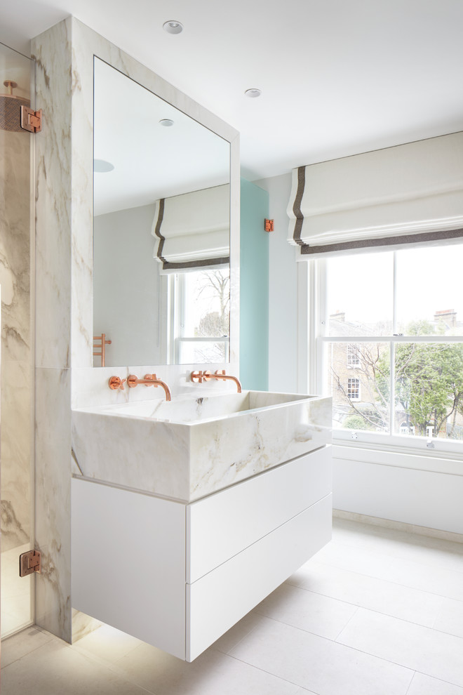 Bild på ett funkis badrum, med marmorkakel, klinkergolv i porslin, släta luckor, vita skåp, vita väggar, ett avlångt handfat, beiget golv och dusch med gångjärnsdörr