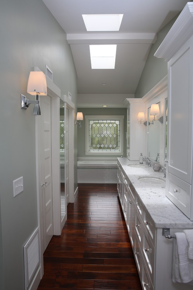 Klassisk inredning av ett mellanstort en-suite badrum, med luckor med infälld panel, vita skåp, ett hörnbadkar, gröna väggar, mörkt trägolv, ett nedsänkt handfat, marmorbänkskiva och brunt golv