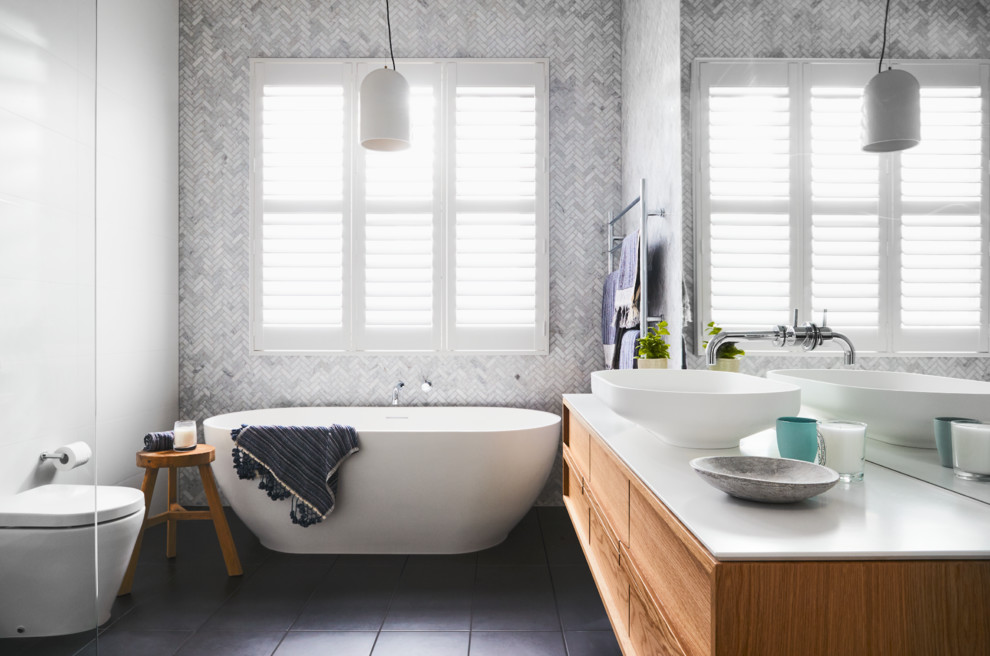 Klassisk inredning av ett vit vitt badrum, med släta luckor, skåp i mellenmörkt trä, ett fristående badkar, vita väggar, ett fristående handfat och grått golv