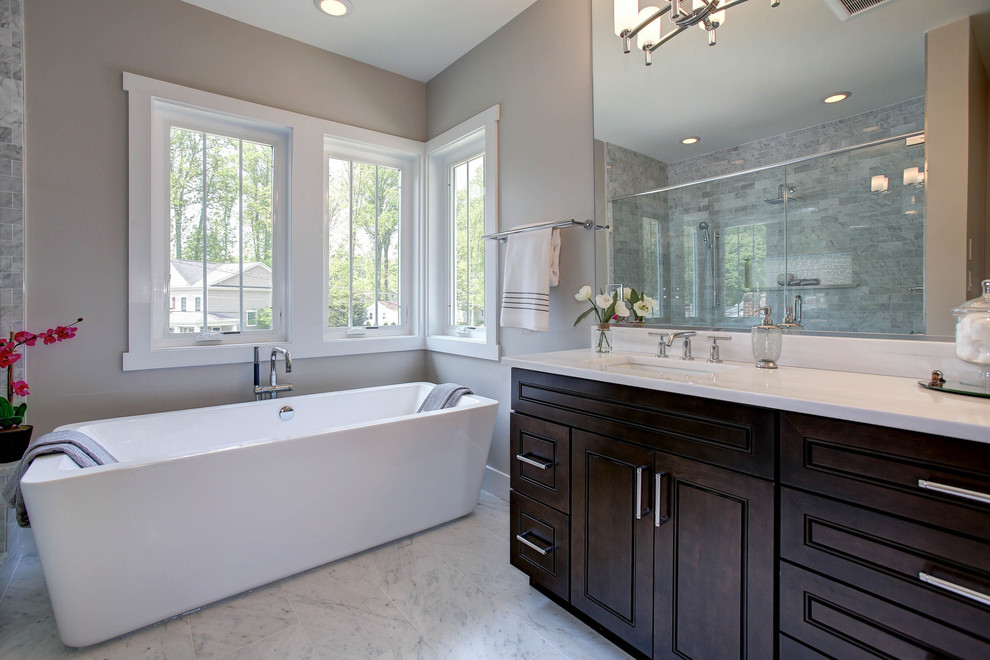 Medium sized traditional ensuite bathroom in DC Metro with raised-panel cabinets, a freestanding bath, an alcove shower, a two-piece toilet, grey tiles, stone tiles, grey walls, marble flooring, a submerged sink, marble worktops and dark wood cabinets.