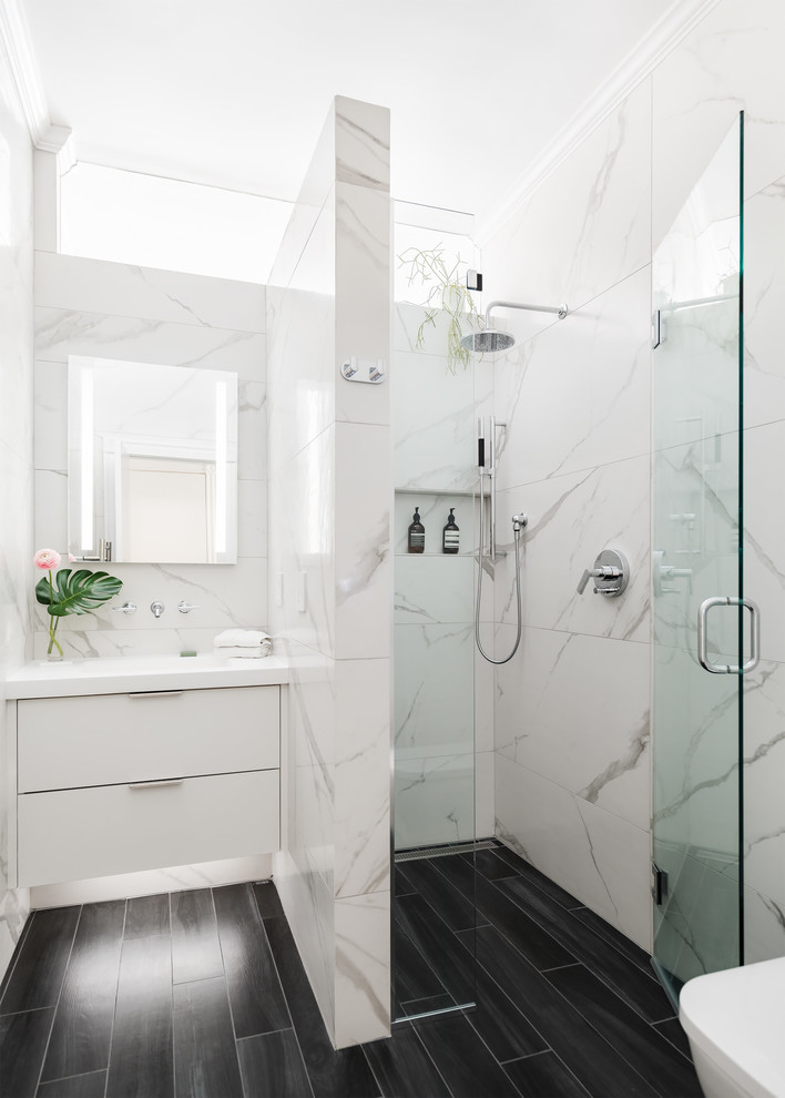 Example of a mid-sized trendy 3/4 porcelain tile and white tile porcelain tile and black floor walk-in shower design in Boston with flat-panel cabinets, white cabinets, white walls, an integrated sink, solid surface countertops, a hinged shower door and white countertops
