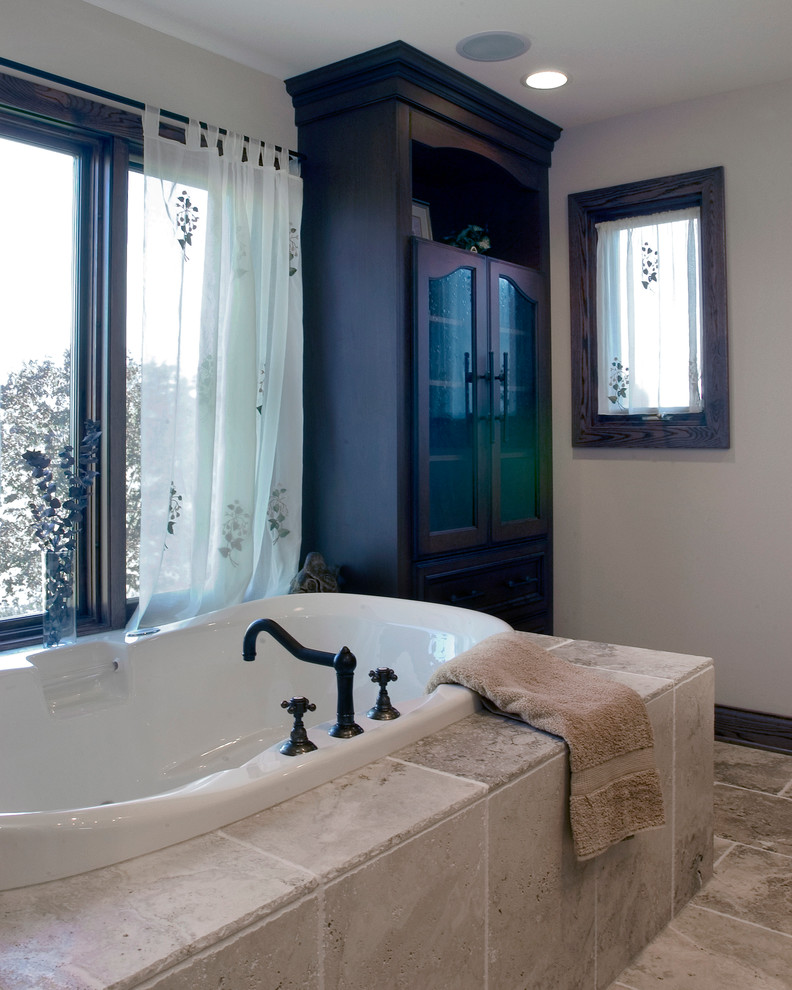 На фото: большая главная ванная комната в стиле рустика с фасадами островного типа, темными деревянными фасадами, накладной ванной, бежевой плиткой, каменной плиткой, бежевыми стенами, полом из известняка и столешницей из известняка
