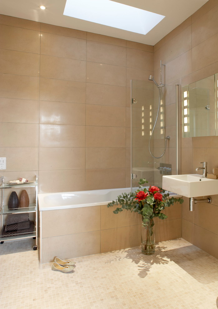 Modern inredning av ett badrum, med ett väggmonterat handfat, ett platsbyggt badkar, en dusch/badkar-kombination, beige kakel, beige väggar och mosaikgolv