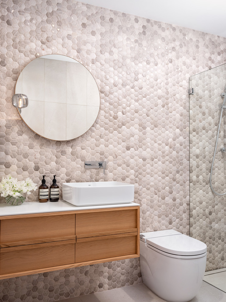 Modernes Badezimmer mit hellbraunen Holzschränken, bodengleicher Dusche, Wandtoilette mit Spülkasten, beigen Fliesen, Mosaikfliesen, beiger Wandfarbe, Aufsatzwaschbecken, grauem Boden und weißer Waschtischplatte in Sydney