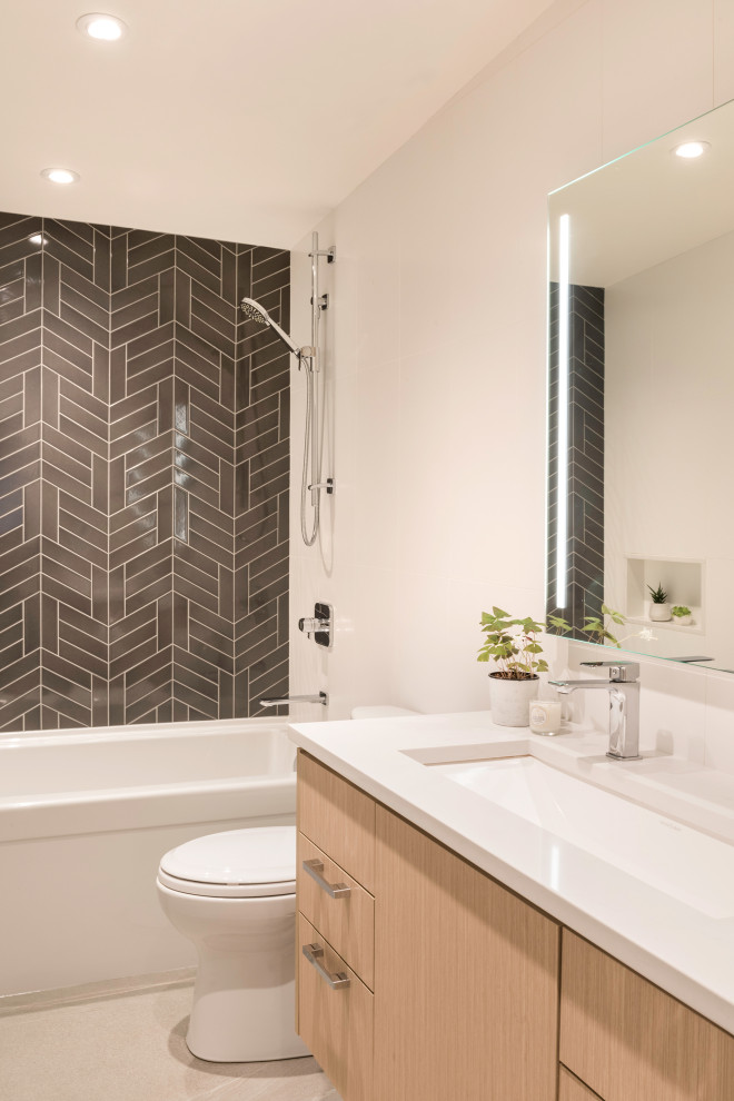 Modernes Badezimmer mit flächenbündigen Schrankfronten, hellen Holzschränken, Badewanne in Nische, Duschbadewanne, schwarzen Fliesen, Unterbauwaschbecken, grauem Boden und weißer Waschtischplatte in Vancouver