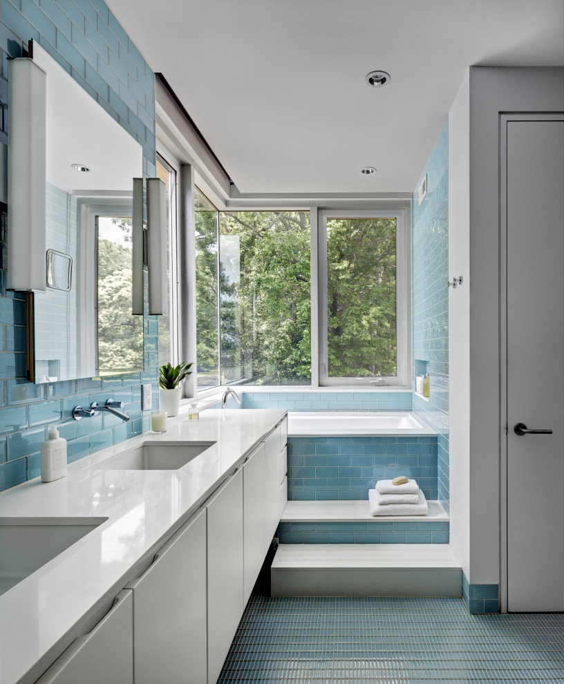 Cette image montre une salle de bain principale design avec un placard à porte plane, des portes de placard blanches, une baignoire encastrée, un mur bleu, un sol en carrelage de céramique, un sol bleu, meuble double vasque et meuble-lavabo suspendu.
