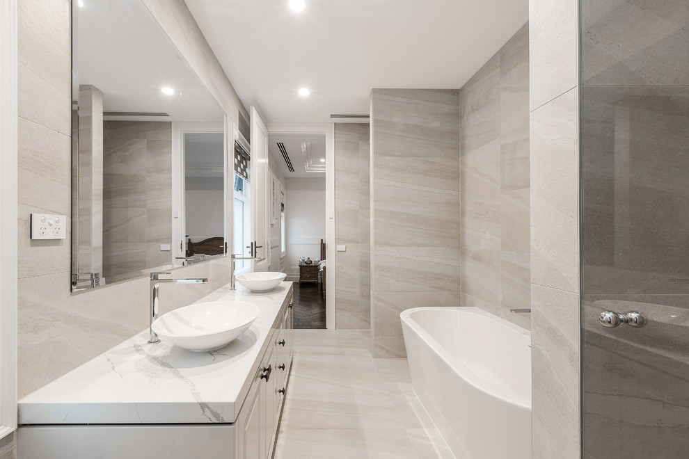 This is an example of a large traditional family bathroom in Melbourne with shaker cabinets, white cabinets, a freestanding bath, beige tiles, marble tiles, marble flooring, a vessel sink, marble worktops, white floors and a hinged door.