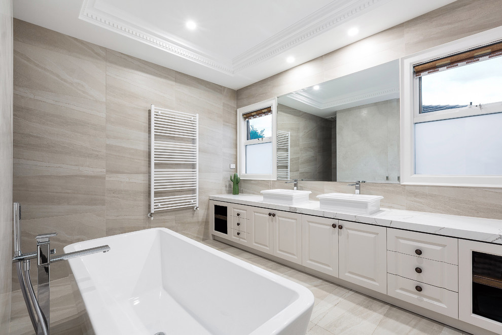 Foto på ett stort vintage en-suite badrum, med vita skåp, ett fristående badkar, beige kakel, marmorkakel, marmorgolv, marmorbänkskiva och vitt golv
