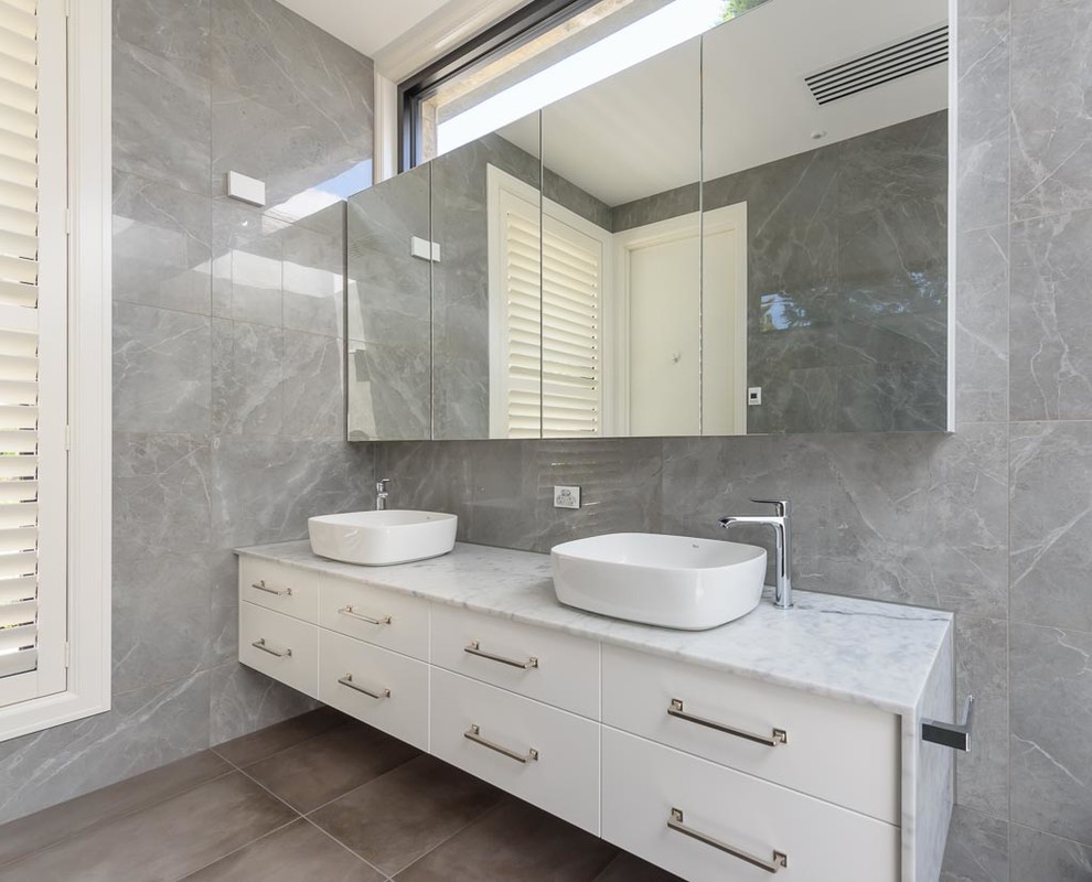 Modern inredning av ett stort flerfärgad flerfärgat badrum, med släta luckor, vita skåp, en öppen dusch, en toalettstol med hel cisternkåpa, grå kakel, porslinskakel, grå väggar, klinkergolv i porslin, ett fristående handfat, marmorbänkskiva, grått golv och med dusch som är öppen