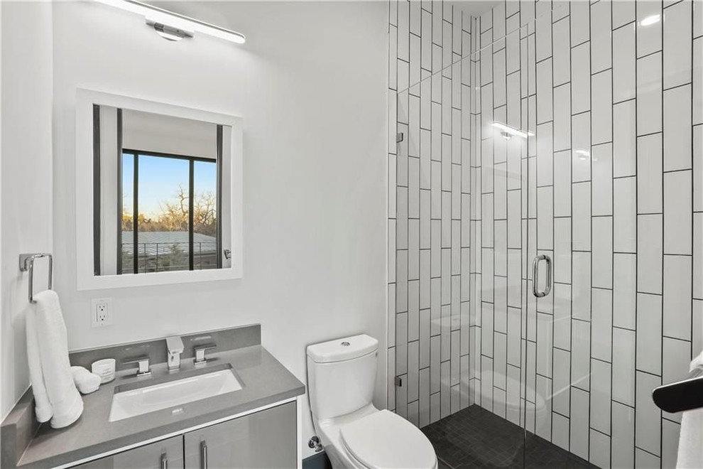 Foto på ett mellanstort funkis grå badrum med dusch, med släta luckor, grå skåp, en dusch i en alkov, en toalettstol med separat cisternkåpa, grå kakel, tunnelbanekakel, vita väggar, ett undermonterad handfat och bänkskiva i akrylsten