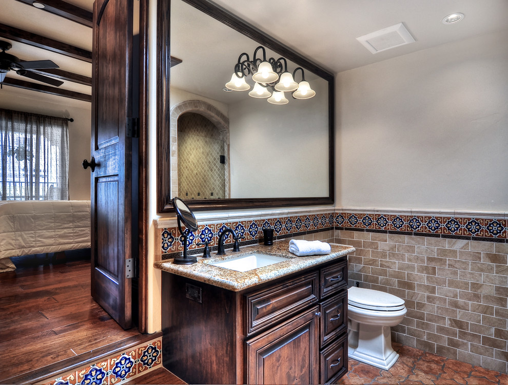This is an example of a medium sized mediterranean ensuite bathroom in Orange County with raised-panel cabinets, brown cabinets, a corner shower, beige tiles, mosaic tiles, white walls, porcelain flooring, a submerged sink, granite worktops, brown floors and a hinged door.