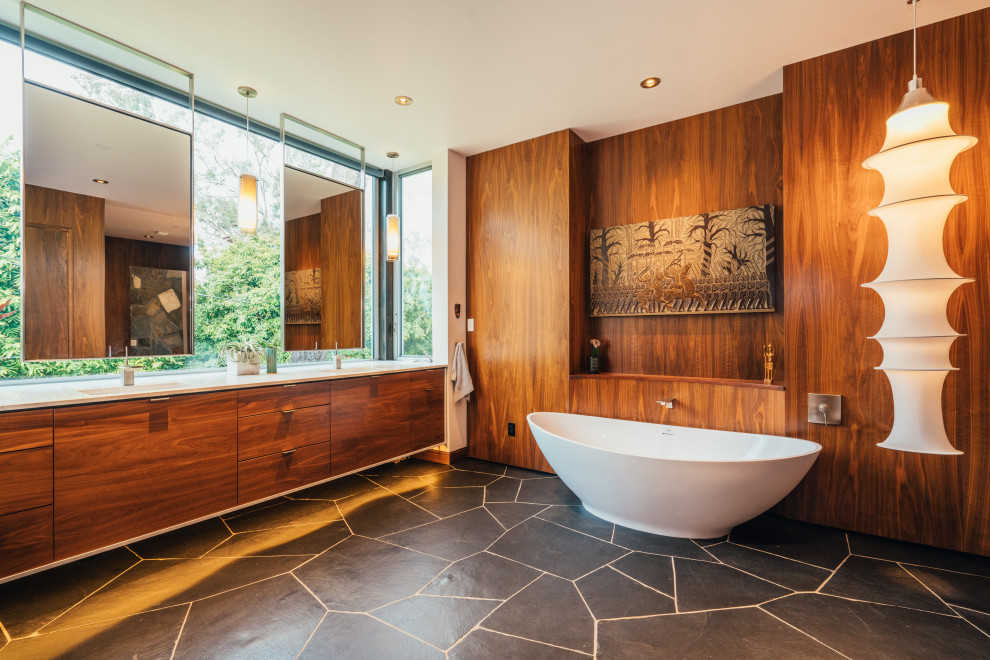 Design ideas for a midcentury ensuite bathroom in San Diego with flat-panel cabinets, medium wood cabinets, a freestanding bath, a submerged sink, grey floors, white worktops, double sinks, a floating vanity unit and wood walls.