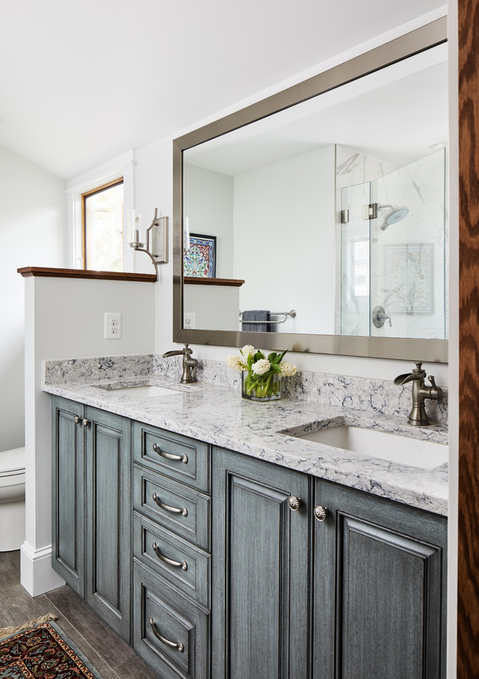 Amerikansk inredning av ett mellanstort grå grått en-suite badrum, med luckor med upphöjd panel, blå skåp, en toalettstol med hel cisternkåpa, vita väggar, klinkergolv i keramik, ett undermonterad handfat, granitbänkskiva och grått golv