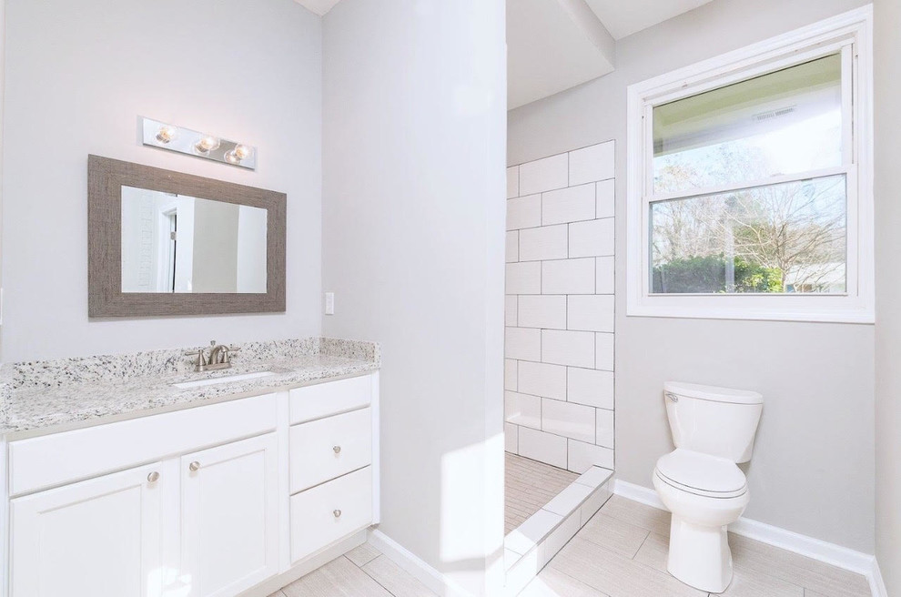 Inspiration for a mid-sized white tile and porcelain tile porcelain tile and gray floor bathroom remodel in Charlotte with recessed-panel cabinets, white cabinets, a two-piece toilet, gray walls, an undermount sink, granite countertops and multicolored countertops