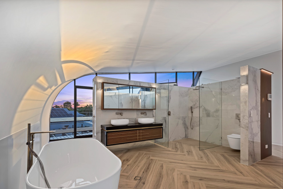 Стильный дизайн: огромная главная ванная комната в современном стиле с отдельно стоящей ванной, угловым душем, инсталляцией, белой плиткой, керамогранитной плиткой, белыми стенами, полом из керамогранита, настольной раковиной, столешницей из искусственного кварца, бежевым полом, открытым душем, черной столешницей, тумбой под две раковины, подвесной тумбой, сводчатым потолком, плоскими фасадами и фасадами цвета дерева среднего тона - последний тренд